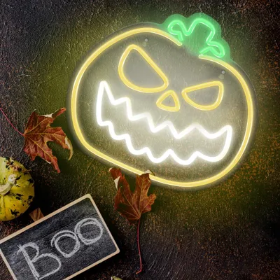 A Halloween-themed neon sign of a jack-o'-lantern is displayed on a dark, textured surface, surrounded by autumn leaves and a small pumpkin.