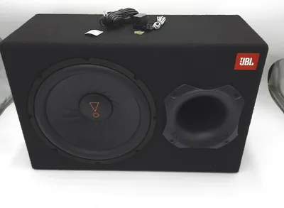A black JBL subwoofer in a box, with cables and accessories on top.
