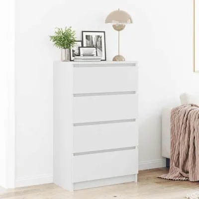 A white dresser with four drawers is shown in a room with a lamp and framed pictures on top.