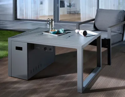 A grey outdoor lounge table with a built-in fire pit, set on a wooden deck next to a grey armchair.