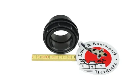 A black ABS tank fitting is shown next to a ruler and a sticker with a koi fish and Japanese architecture.