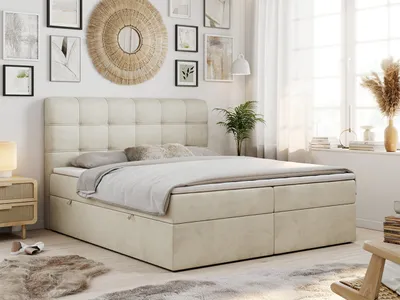 A bedroom scene with a beige box spring bed as the main focus, decorated with wall art and plants.