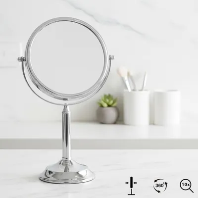 A silver makeup mirror on a white countertop with a marble pattern.