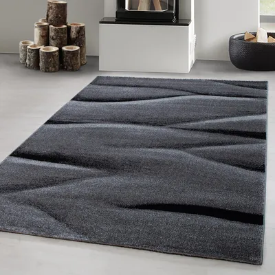 A modern abstract rug in shades of gray and black, placed on a light gray floor.