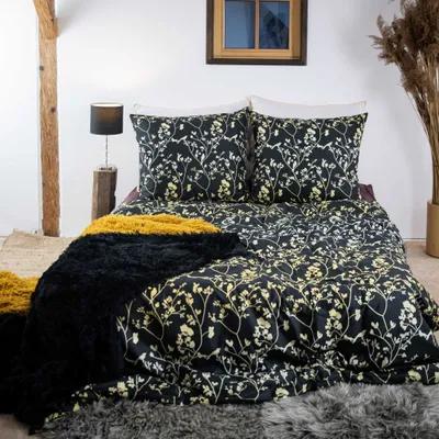 A bed with black and gold floral patterned bedding, a black fluffy throw blanket, and a yellow throw blanket.