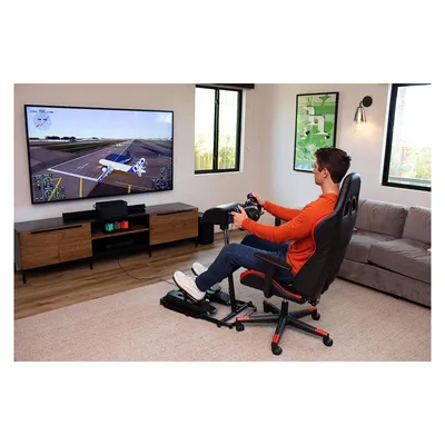 A man is playing a flight simulator game using a racing wheel and pedals setup in a living room.