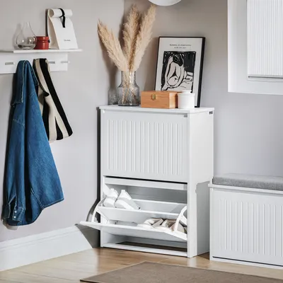 A white shoe cabinet with two flip-down drawers is shown in a hallway setting, with a denim jacket and a striped scarf hanging on a wall rack.