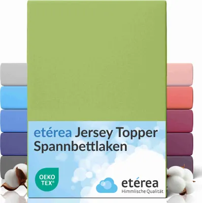 A product image showcasing a green fitted sheet with multiple other fitted sheets in various colors stacked behind it. Cotton bolls are visible in the foreground.