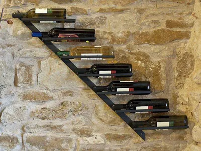 A metal wine rack mounted on a stone wall, holding several bottles of wine.