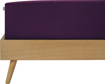 A close-up view of a mattress with a purple fitted sheet on a wooden bed frame.