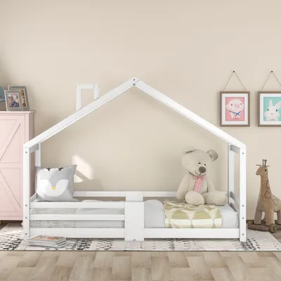 A white house-shaped bed for children, with a teddy bear and a giraffe toy on it, in a room with light beige walls.