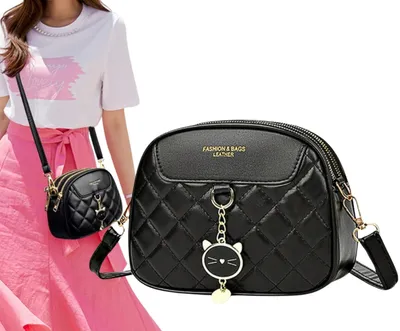 A person is modeling a small black quilted crossbody bag with a cat charm.