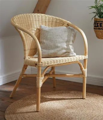 A rattan chair with a cushion sits on a jute rug in a room with wooden floors and a sloped ceiling.