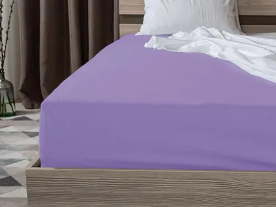 A close-up view of a bed with a purple fitted sheet and a white crumpled sheet and pillow.