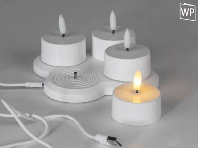A white charging station with four white LED tea lights, one of which is lit.