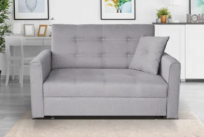 A gray sofa is shown in a well-lit room with a desk and pictures in the background.