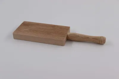 A wooden gnocchi board with a handle, placed on a light gray background.