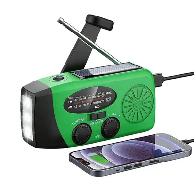 A green emergency radio with a solar panel, LED flashlight, and antenna is shown with a smartphone connected to it, suggesting it can charge the phone.
