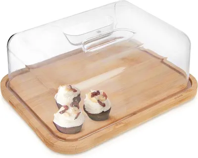 A clear, well-lit studio shot of a bamboo cutting board with a clear plastic dome lid, featuring three small cupcakes.