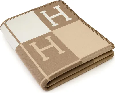 A folded blanket with a checkered pattern and the letter 'H' on it.