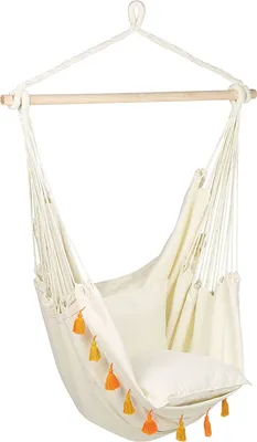 A beige hammock chair with orange and yellow tassels hanging from a wooden bar.
