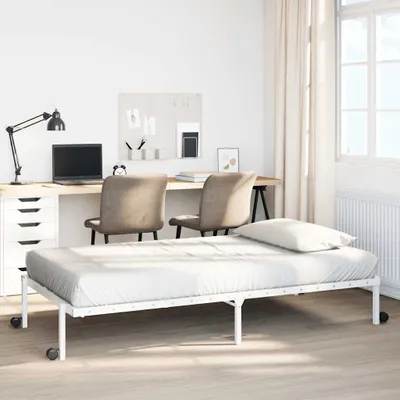 A white foldable bed frame with a mattress and pillow in a room with a desk and chairs.