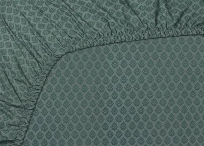 A close-up view of a green fitted sheet with a repeating leaf pattern.