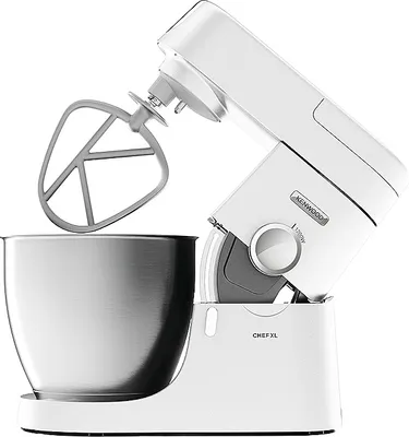 A white Kenwood Chef XL food processor with a silver mixing bowl and beater attachment, shown from a side angle against a white background.