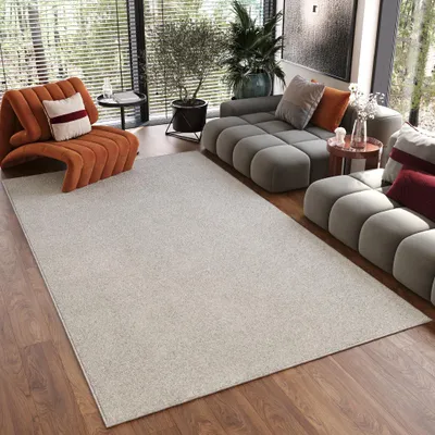 A modern living room with a large cream rug, an orange accent chair, and a modular gray sofa.