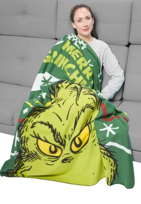 A woman sitting on a couch, wrapped in a Grinch-themed blanket.