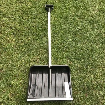 A black shovel with a white handle lies on a green grassy lawn.