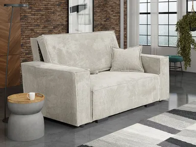 A beige sofa with a pillow is shown in a living room setting with a brick wall and a window in the background.