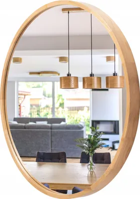 A round wooden mirror reflects a modern living and dining area with furniture and pendant lights.