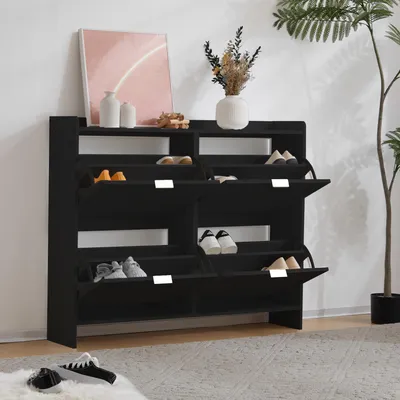 A black shoe cabinet with multiple shelves and flip-down doors, filled with shoes, is shown in a room setting.