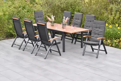 An outdoor dining set with a table and chairs on a patio, surrounded by greenery and flowers.