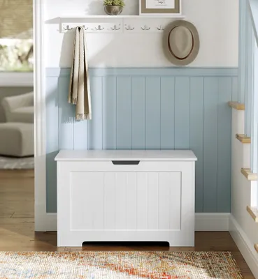 A hallway with a white storage bench, a shelf with a hat and plant, and a blanket hanging on hooks.