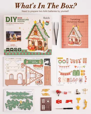A flat lay of a DIY miniature Christmas house kit, showing the box, instruction booklet, and all the unassembled parts.