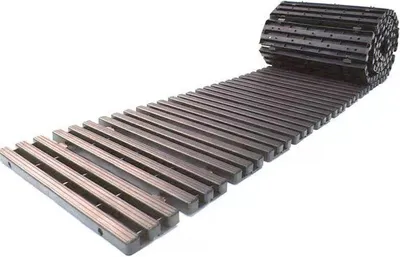 A dark gray, slatted walkway or track is unrolled on a white background, with one end still rolled up.
