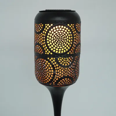 A close-up view of a black solar-powered garden light with intricate cut-out patterns that emit a warm, orange glow.