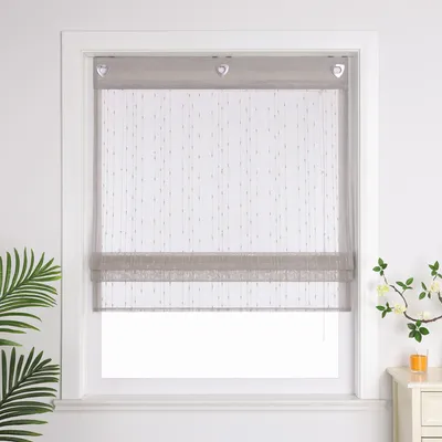 A window with a gray roman shade, decorated with small dangling beads, is shown in a room with a plant on the left and a nightstand with a vase of flowers and a glass of juice on the right.