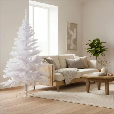 A white artificial Christmas tree is set up in a living room next to a couch and coffee table.