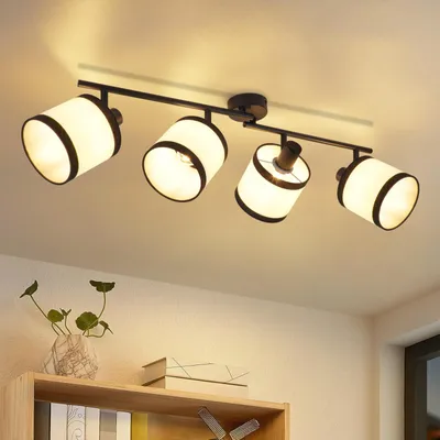 A four-light ceiling spotlight fixture with fabric shades, mounted on a ceiling above a shelf with a vase and books.