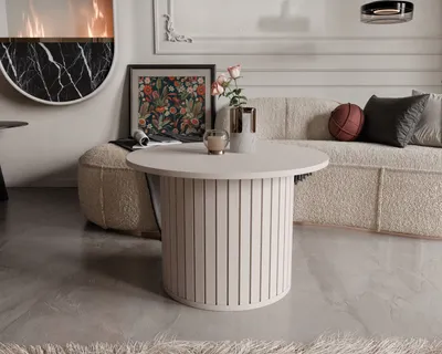 A round coffee table with a ribbed base is placed in a living room setting, next to a sofa and a fireplace.