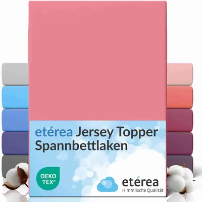 A pink fitted sheet is displayed prominently, with other colored sheets stacked behind it on the left and right sides. Cotton bolls are visible in the lower left corner.