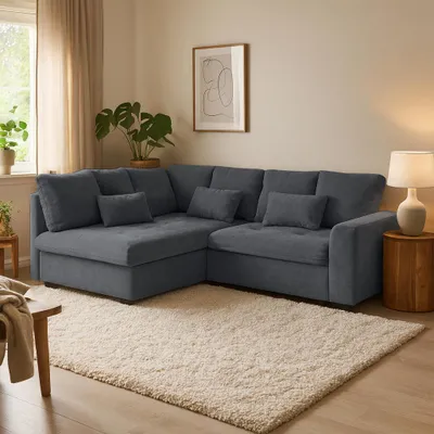 A sectional sofa is arranged in a living room setting, with a rug, a side table, a lamp, and a plant.