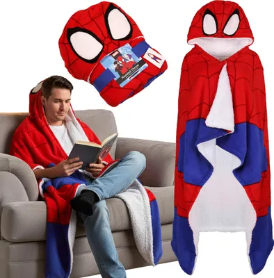 A man is sitting on a couch reading a book while wearing a Spider-Man hooded blanket.