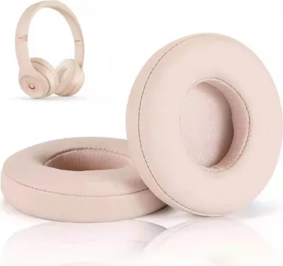 A pair of replacement ear pads for headphones, with a pair of gold headphones in the background.