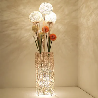 A floor lamp with a woven rattan base and four spherical light fixtures resembling dandelions, with some decorative artificial flowers and leaves.
