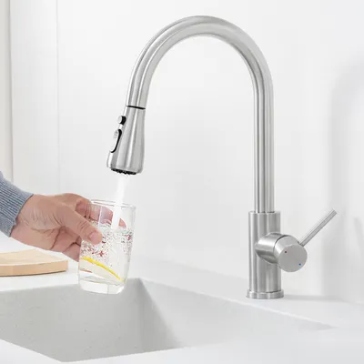 A hand is filling a glass with water from a kitchen faucet.
