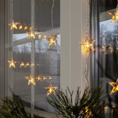 Star-shaped LED lights hanging in a window, with pine branches in the foreground.